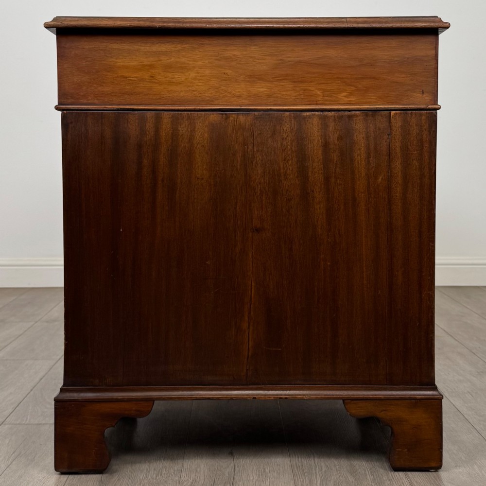 A 20th-century mahogany twin pedestal desk featuring nine drawers with brass drop handles and bracket feet. View VII