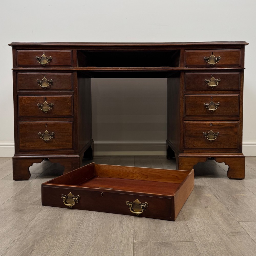 A 20th-century mahogany twin pedestal desk featuring nine drawers with brass drop handles and bracket feet. View X