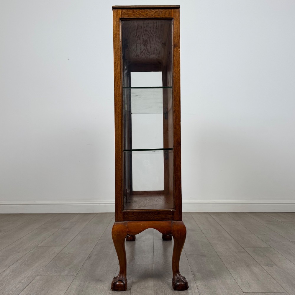 An antique 20th-century oak display cabinet featuring twin glazed doors, glass interior shelves, a carved top frieze, and cabriole legs ending in ball-and-claw feet. View V