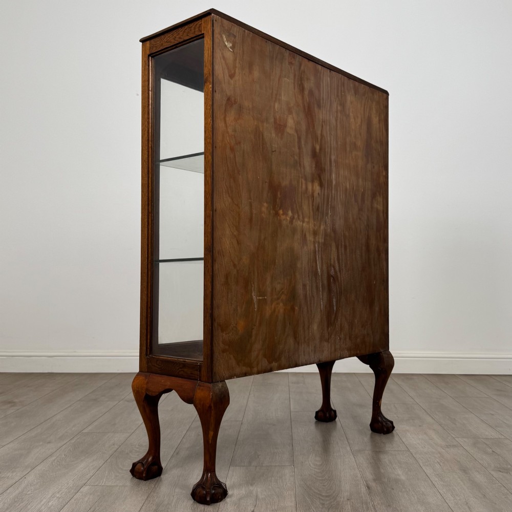 An antique 20th-century oak display cabinet featuring twin glazed doors, glass interior shelves, a carved top frieze, and cabriole legs ending in ball-and-claw feet. View VI
