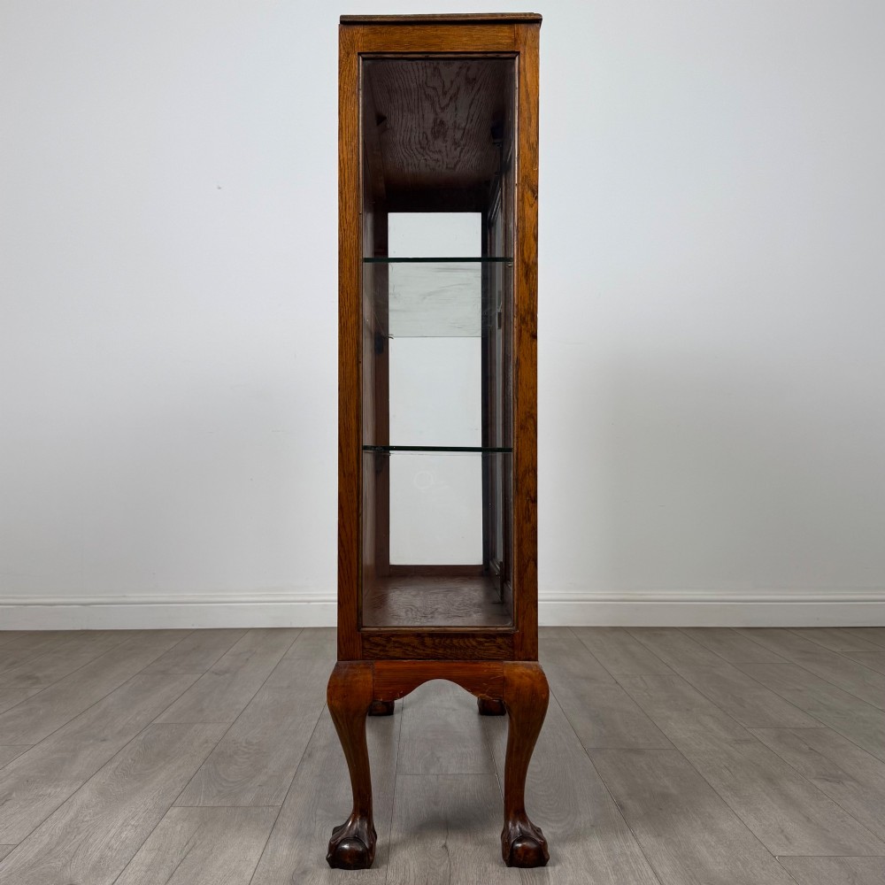 An antique 20th-century oak display cabinet featuring twin glazed doors, glass interior shelves, a carved top frieze, and cabriole legs ending in ball-and-claw feet. View IX