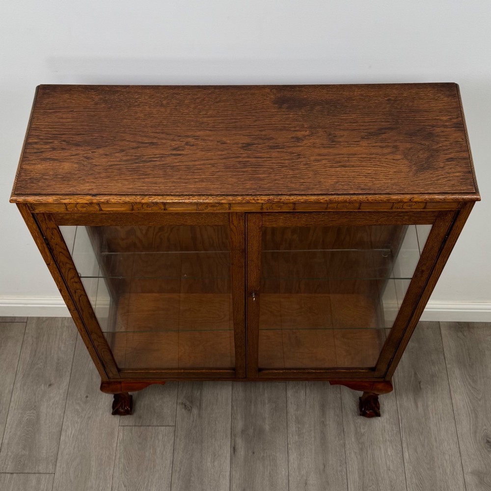 An antique 20th-century oak display cabinet featuring twin glazed doors, glass interior shelves, a carved top frieze, and cabriole legs ending in ball-and-claw feet. View XI