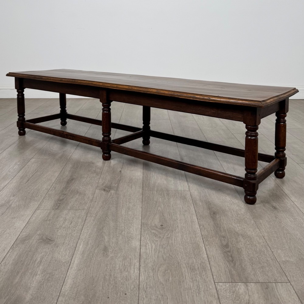 A long dark oak bench featuring six turned legs, perimeter stretchers, and a multi-coloured striped upholstered seat cushion. View III