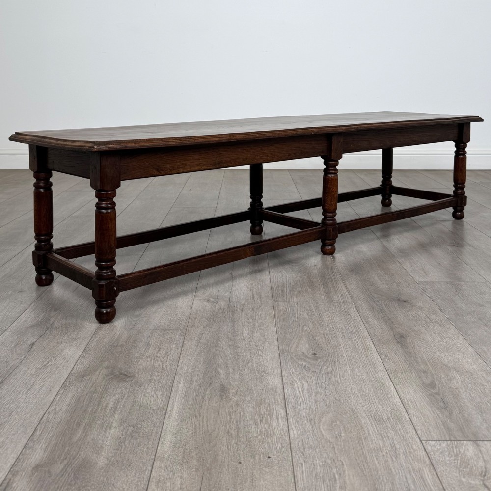 A long dark oak bench featuring six turned legs, perimeter stretchers, and a multi-coloured striped upholstered seat cushion. View V