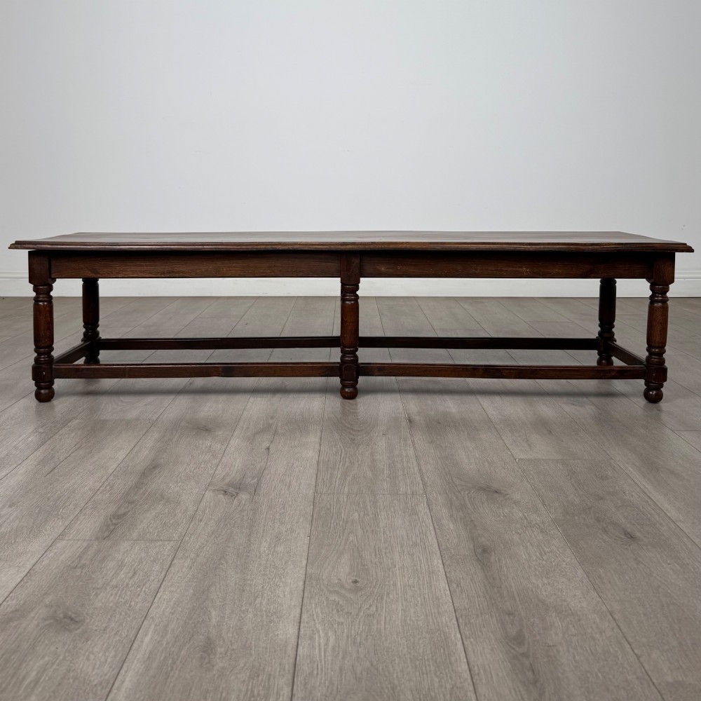 A long dark oak bench featuring six turned legs, perimeter stretchers, and a multi-coloured striped upholstered seat cushion. View VI