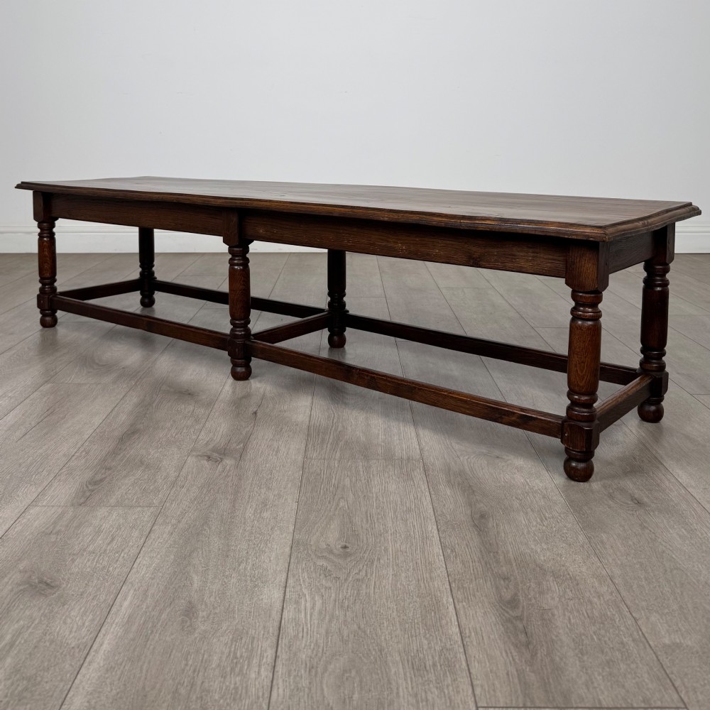 A long dark oak bench featuring six turned legs, perimeter stretchers, and a multi-coloured striped upholstered seat cushion. View VII