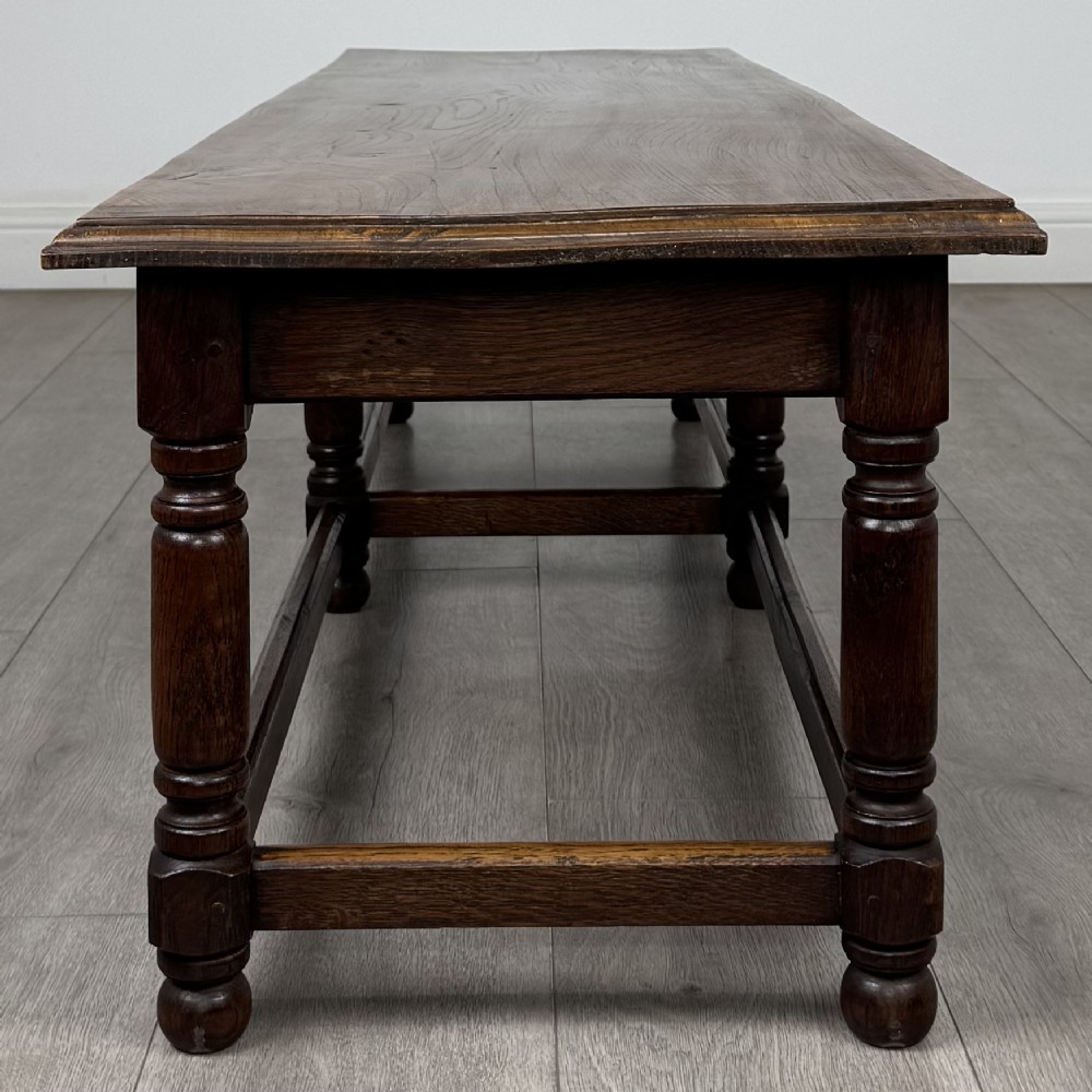 A long dark oak bench featuring six turned legs, perimeter stretchers, and a multi-coloured striped upholstered seat cushion. View VIII