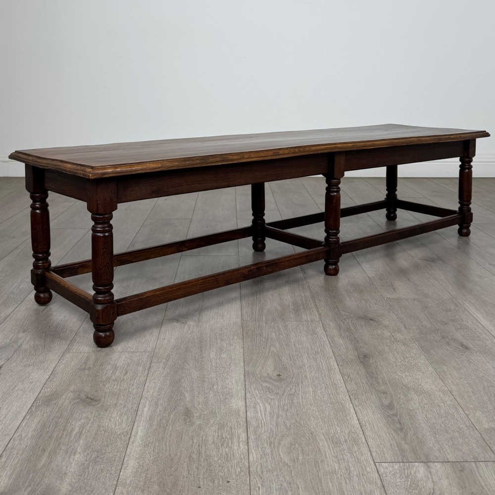 A long dark oak bench featuring six turned legs, perimeter stretchers, and a multi-coloured striped upholstered seat cushion. View IX