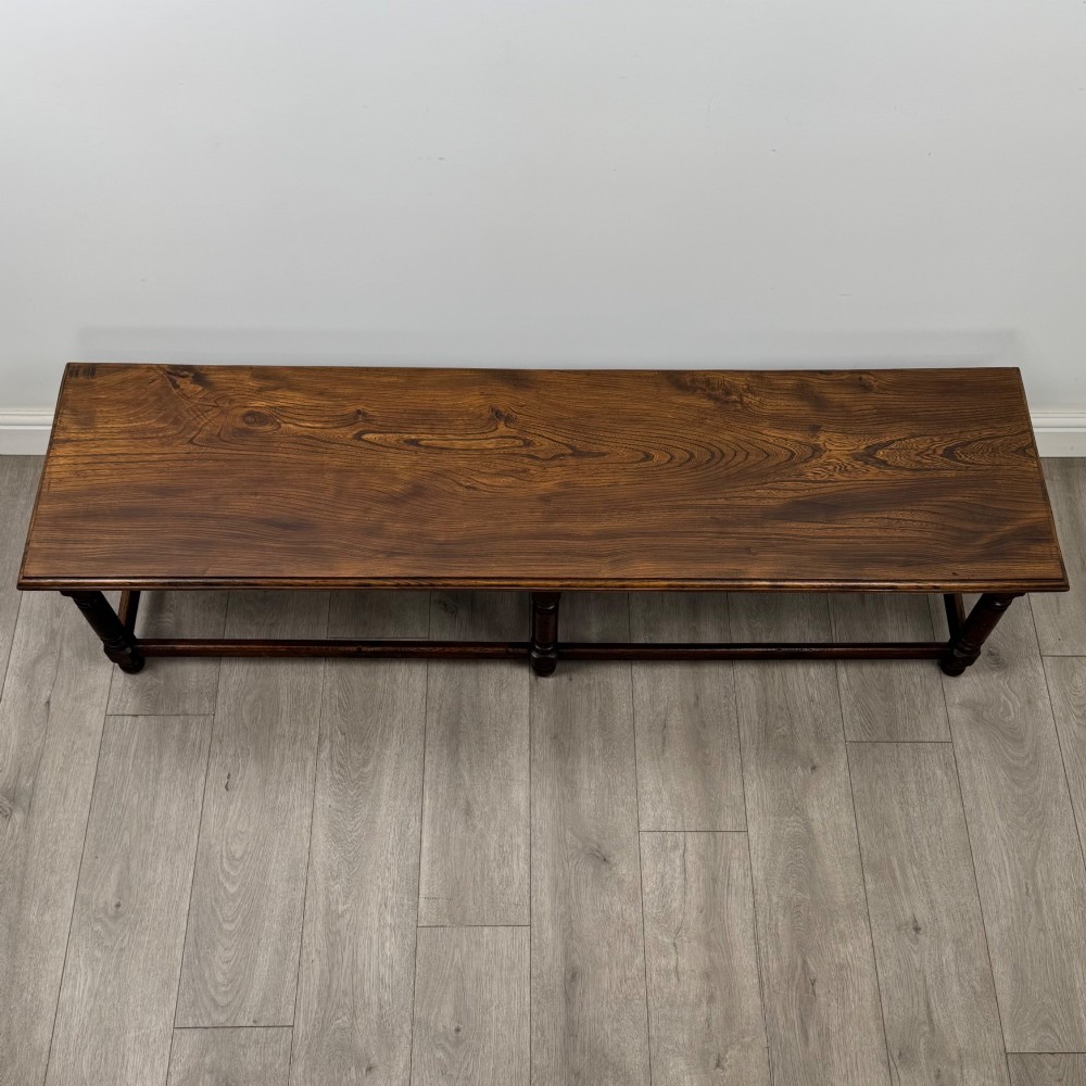 A long dark oak bench featuring six turned legs, perimeter stretchers, and a multi-coloured striped upholstered seat cushion. View XI