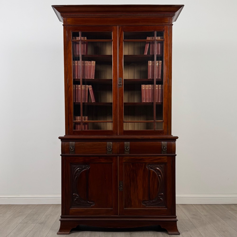 An antique 20th-century mahogany glazed bookcase featuring two upper glass doors, twin middle drawers, and carved lower cupboard doors.