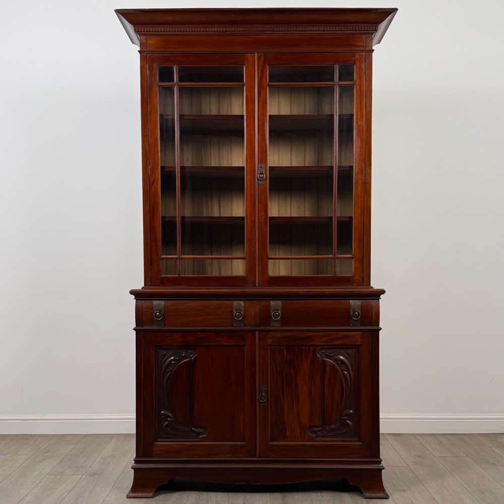 An antique 20th-century mahogany glazed bookcase featuring two upper glass doors, twin middle drawers, and carved lower cupboard doors. View II