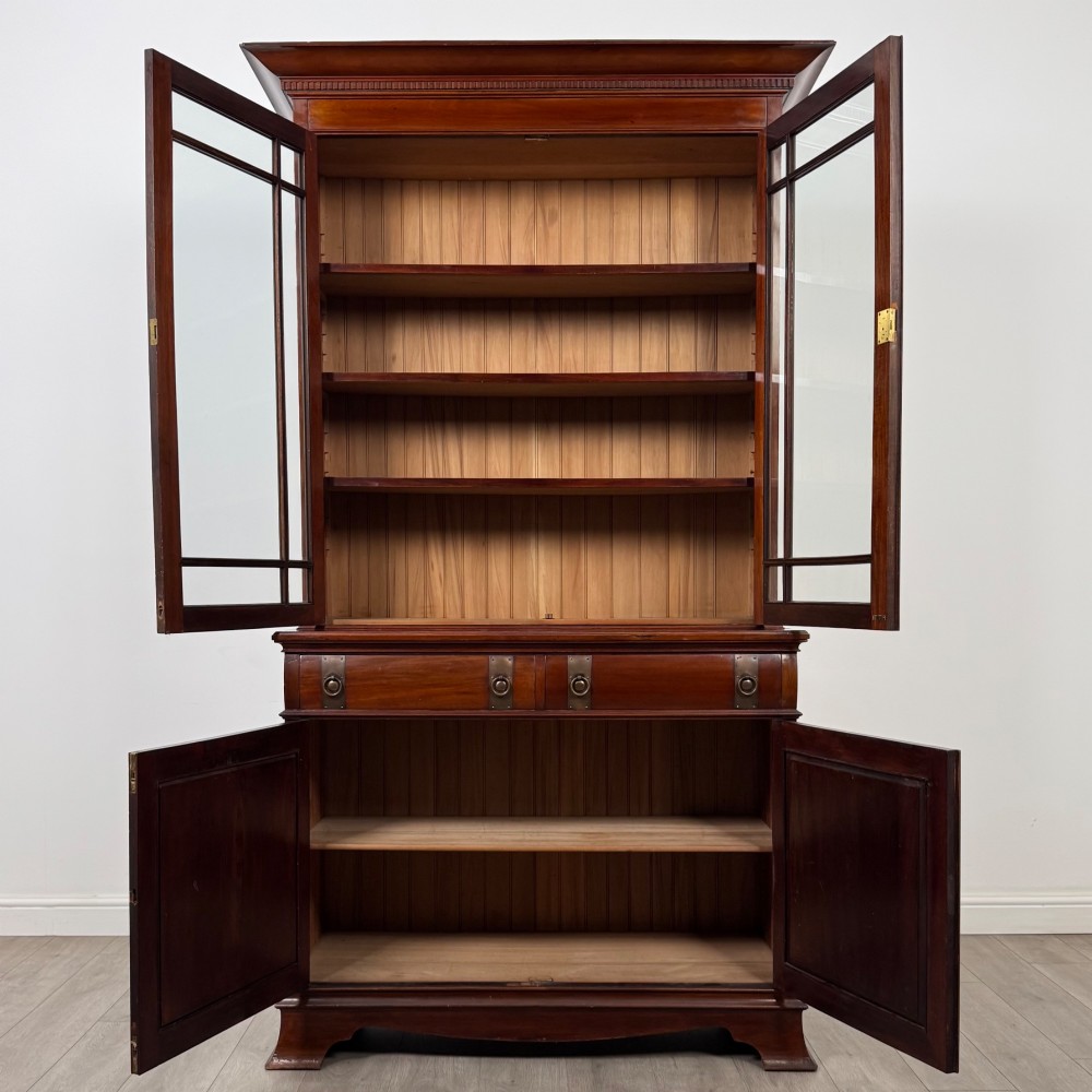 An antique 20th-century mahogany glazed bookcase featuring two upper glass doors, twin middle drawers, and carved lower cupboard doors. View III