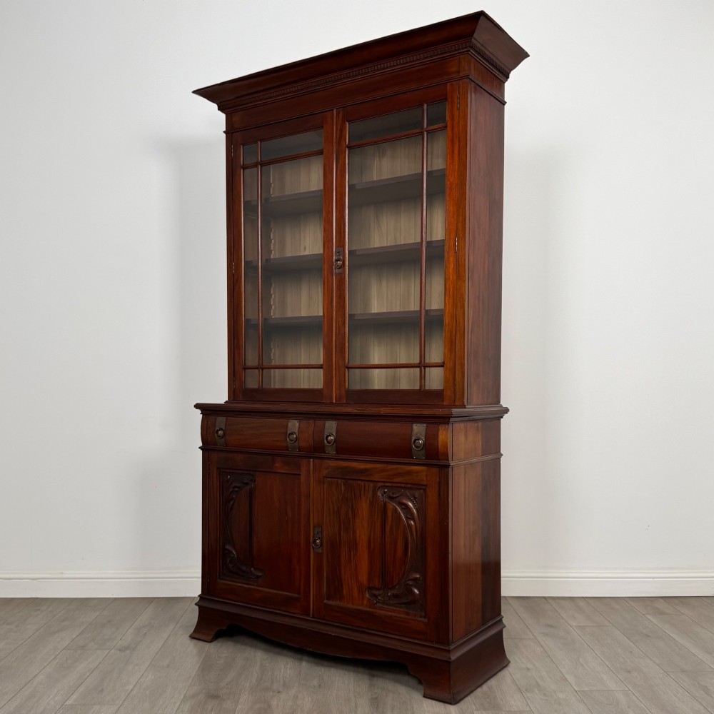 An antique 20th-century mahogany glazed bookcase featuring two upper glass doors, twin middle drawers, and carved lower cupboard doors. View IV