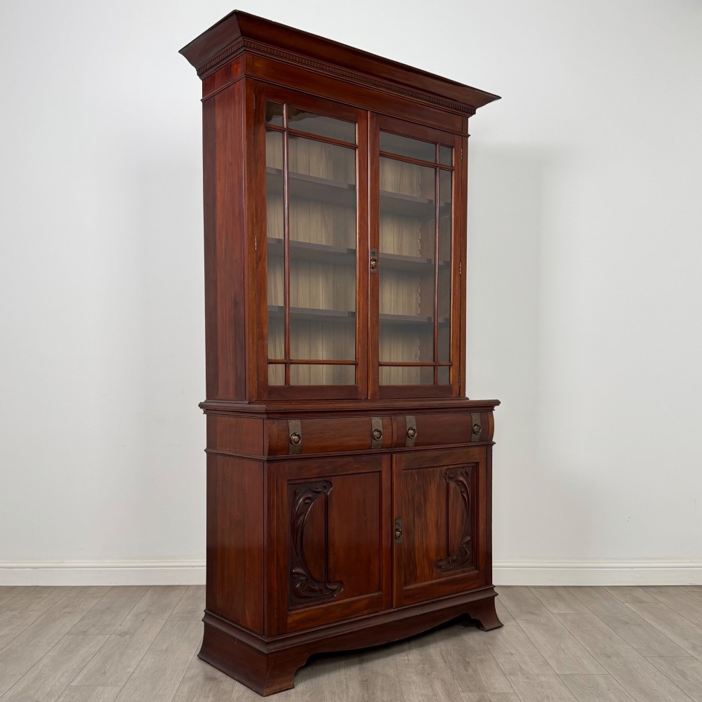 An antique 20th-century mahogany glazed bookcase featuring two upper glass doors, twin middle drawers, and carved lower cupboard doors. View X