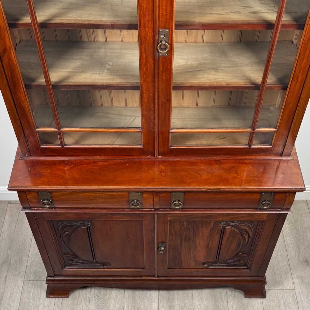 An antique 20th-century mahogany glazed bookcase featuring two upper glass doors, twin middle drawers, and carved lower cupboard doors. View XI