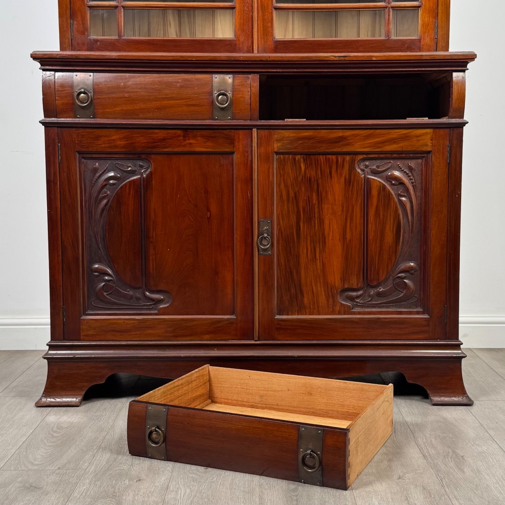 An antique 20th-century mahogany glazed bookcase featuring two upper glass doors, twin middle drawers, and carved lower cupboard doors. View XII