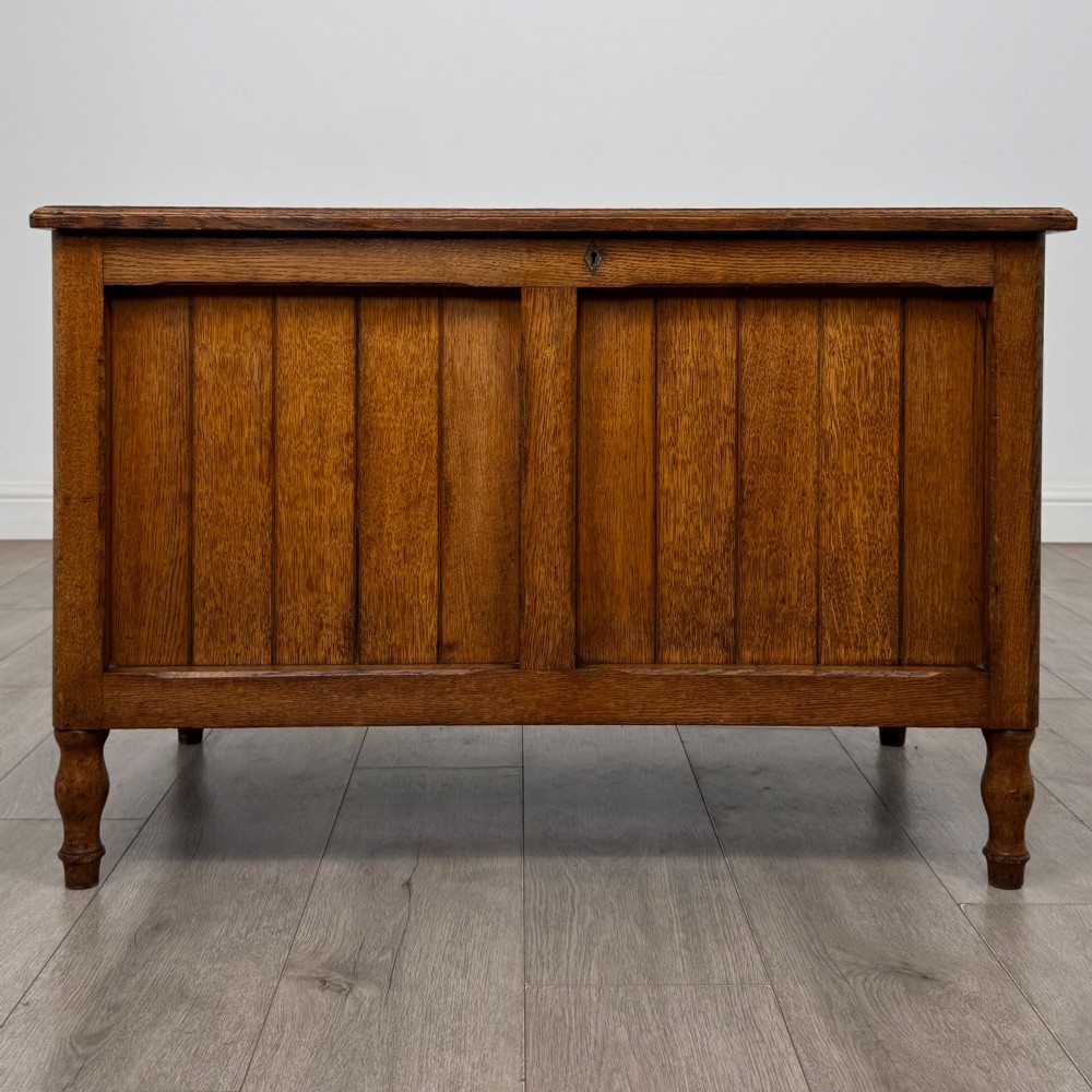 A golden oak Arts and Crafts blanket box featuring vertical panelled sides, a central escutcheon keyhole, and turned legs.