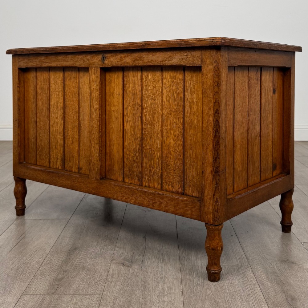 A golden oak Arts and Crafts blanket box featuring vertical panelled sides, a central escutcheon keyhole, and turned legs. View II