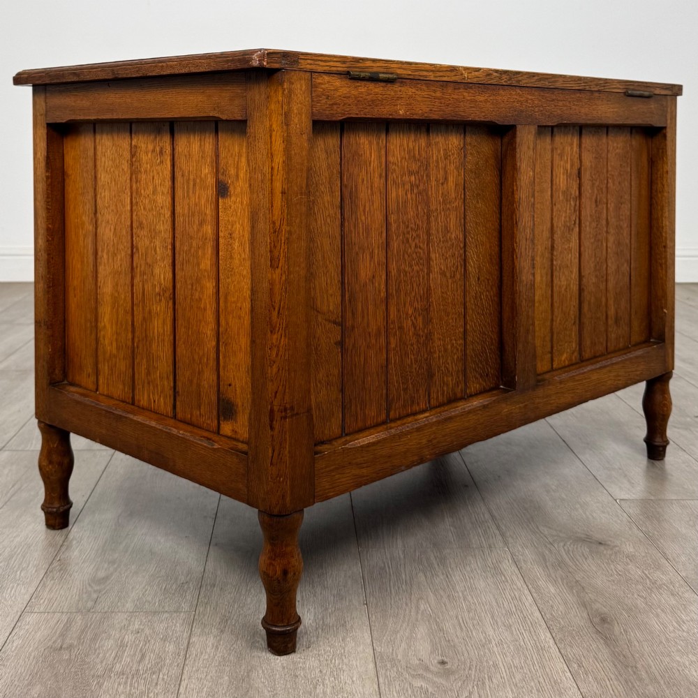 A golden oak Arts and Crafts blanket box featuring vertical panelled sides, a central escutcheon keyhole, and turned legs. View IV
