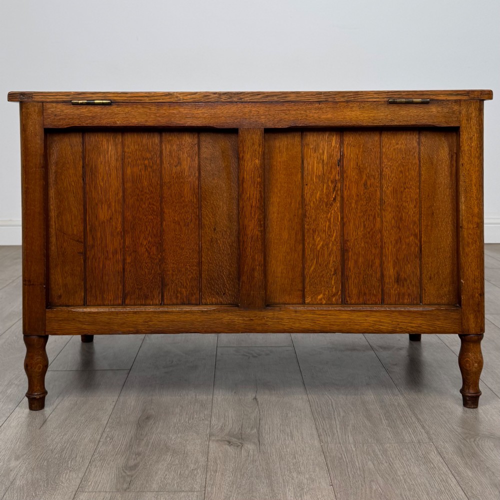 A golden oak Arts and Crafts blanket box featuring vertical panelled sides, a central escutcheon keyhole, and turned legs. View V