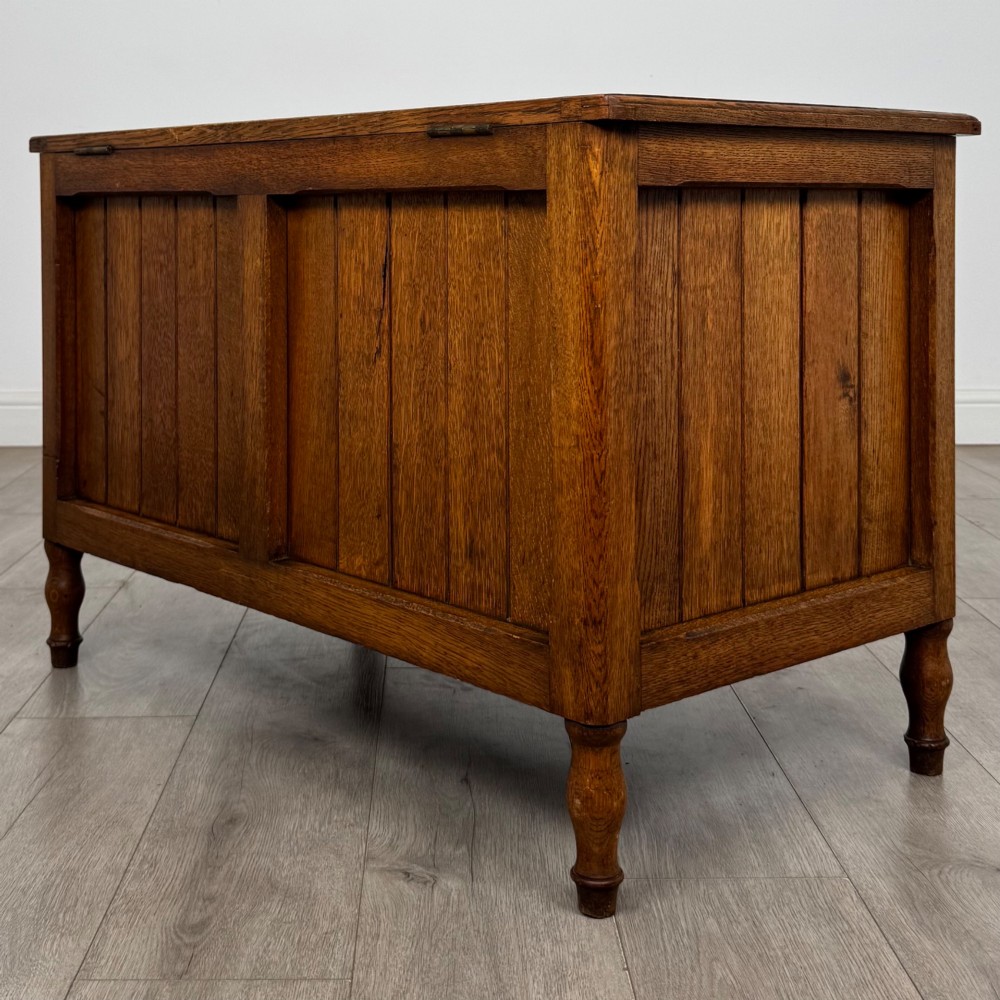 A golden oak Arts and Crafts blanket box featuring vertical panelled sides, a central escutcheon keyhole, and turned legs. View VI