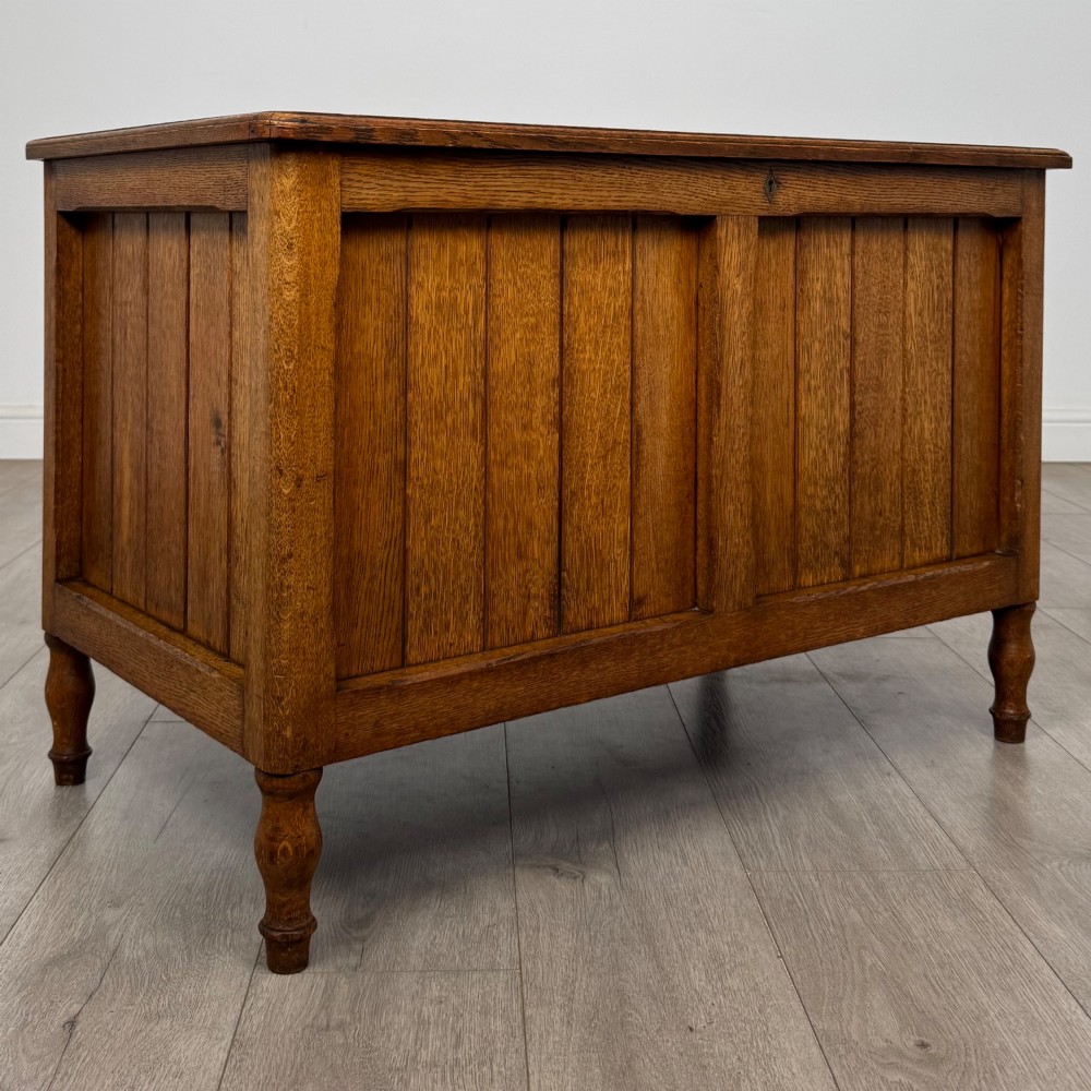 A golden oak Arts and Crafts blanket box featuring vertical panelled sides, a central escutcheon keyhole, and turned legs. View VIII