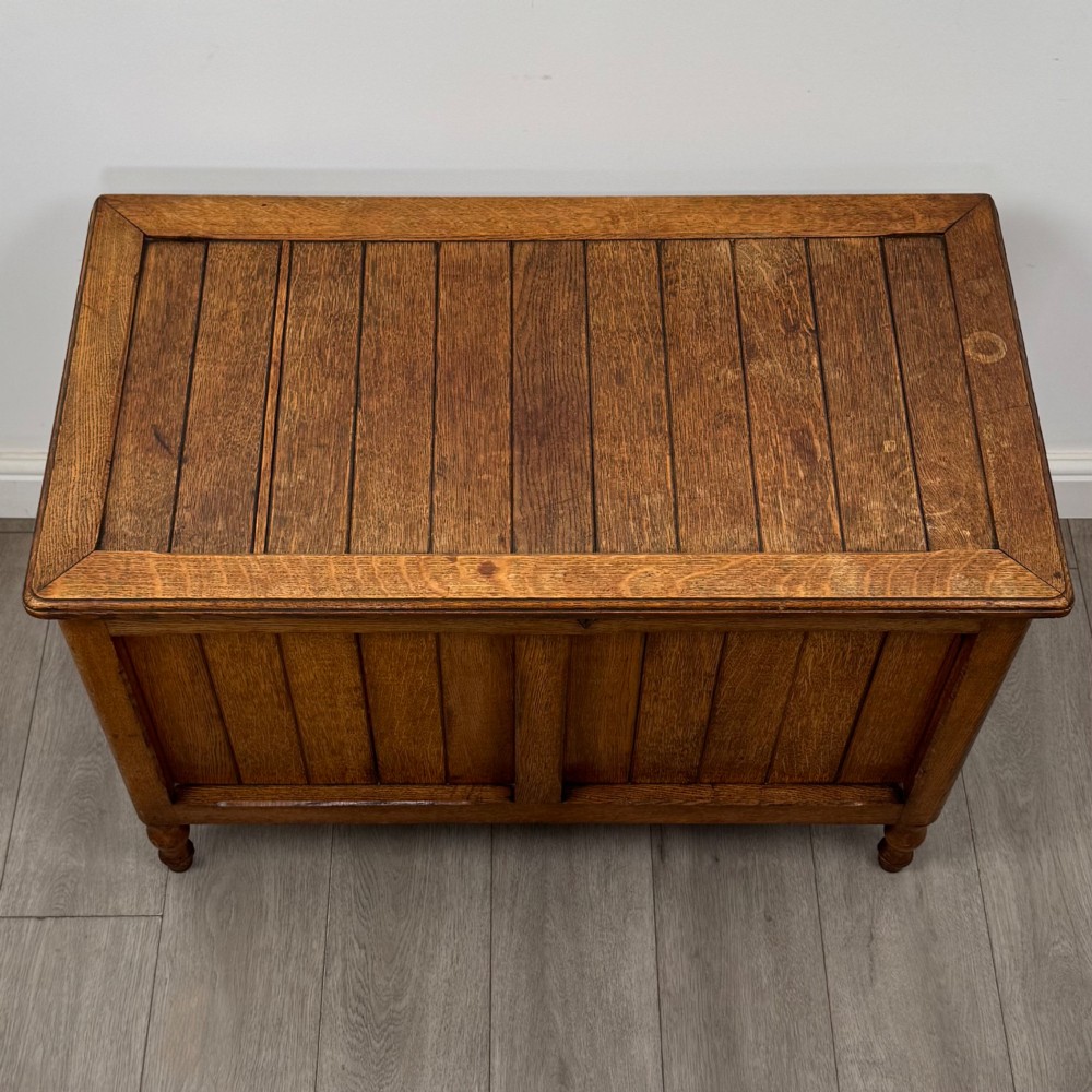 A golden oak Arts and Crafts blanket box featuring vertical panelled sides, a central escutcheon keyhole, and turned legs. View IX