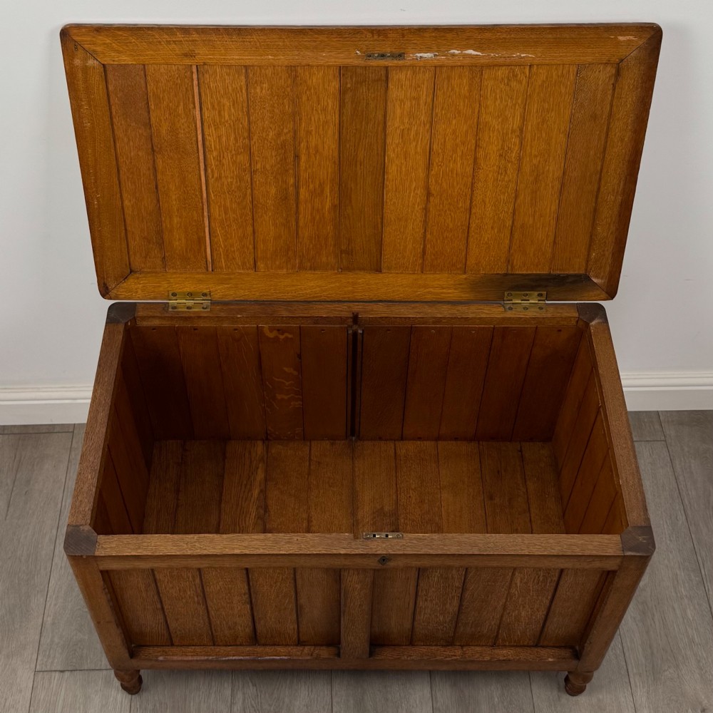 A golden oak Arts and Crafts blanket box featuring vertical panelled sides, a central escutcheon keyhole, and turned legs. View X