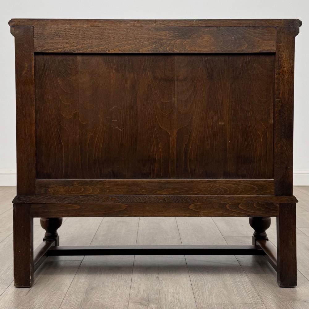 A dark oak cupboard featuring two relief-carved heraldic door panels above two drawers, supported by turned legs and stretchers. View VI