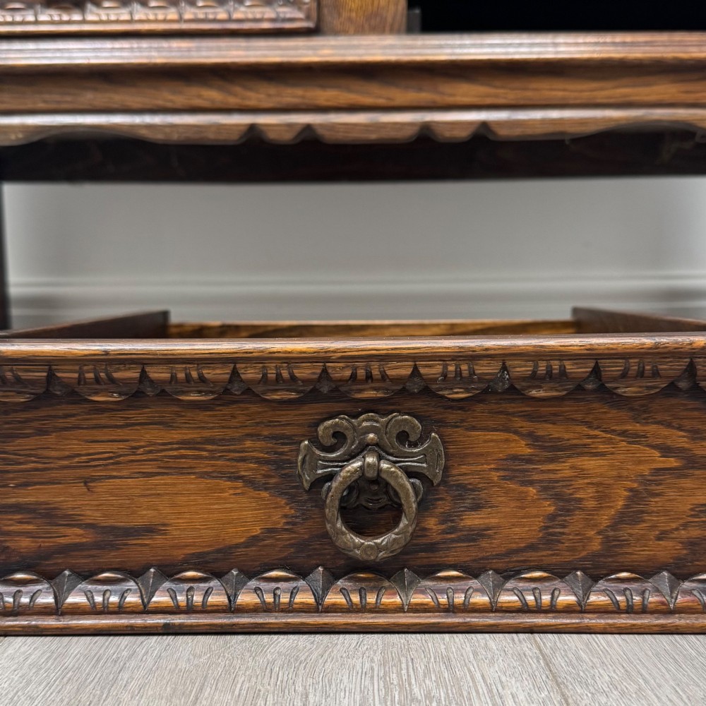 A dark oak cupboard featuring two relief-carved heraldic door panels above two drawers, supported by turned legs and stretchers. View XII