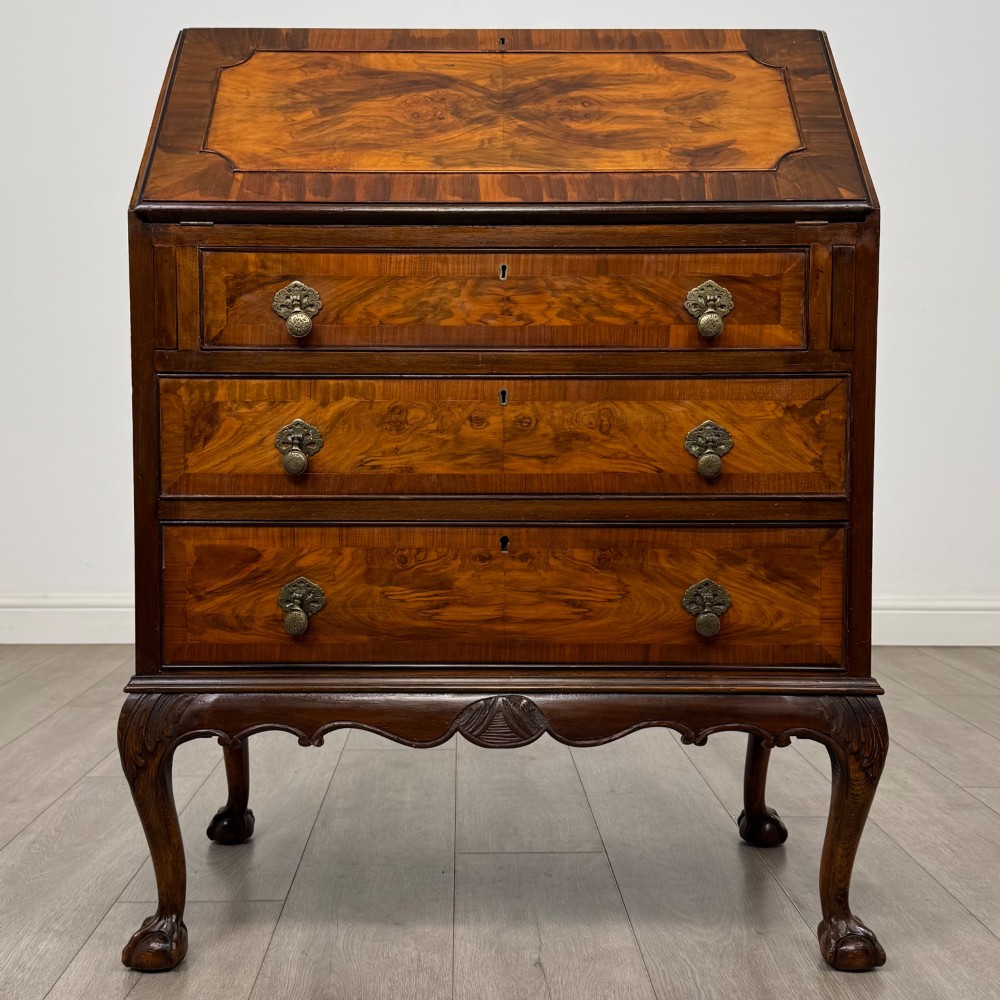 An antique Edwardian figured walnut writing bureau with a slant-front lid, three long drawers, brass handles, and carved cabriole legs on claw-and-ball feet.
