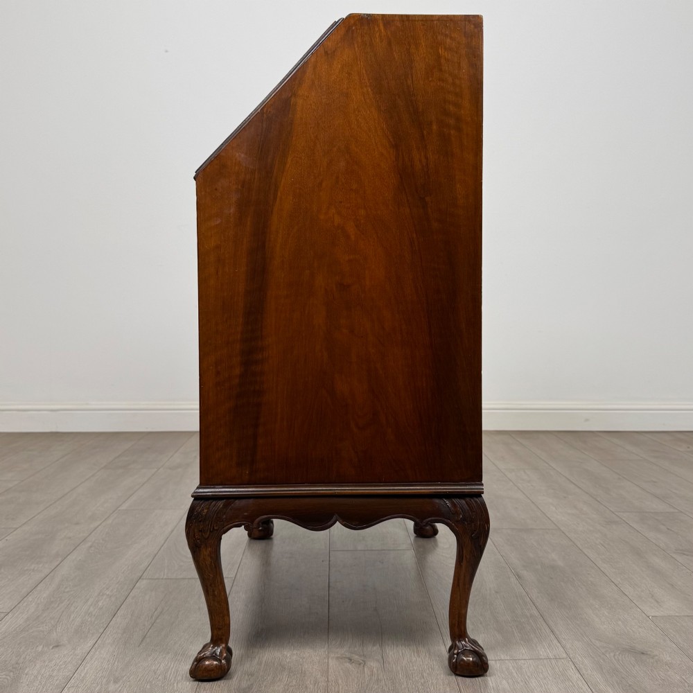 An antique Edwardian figured walnut writing bureau with a slant-front lid, three long drawers, brass handles, and carved cabriole legs on claw-and-ball feet. View IV