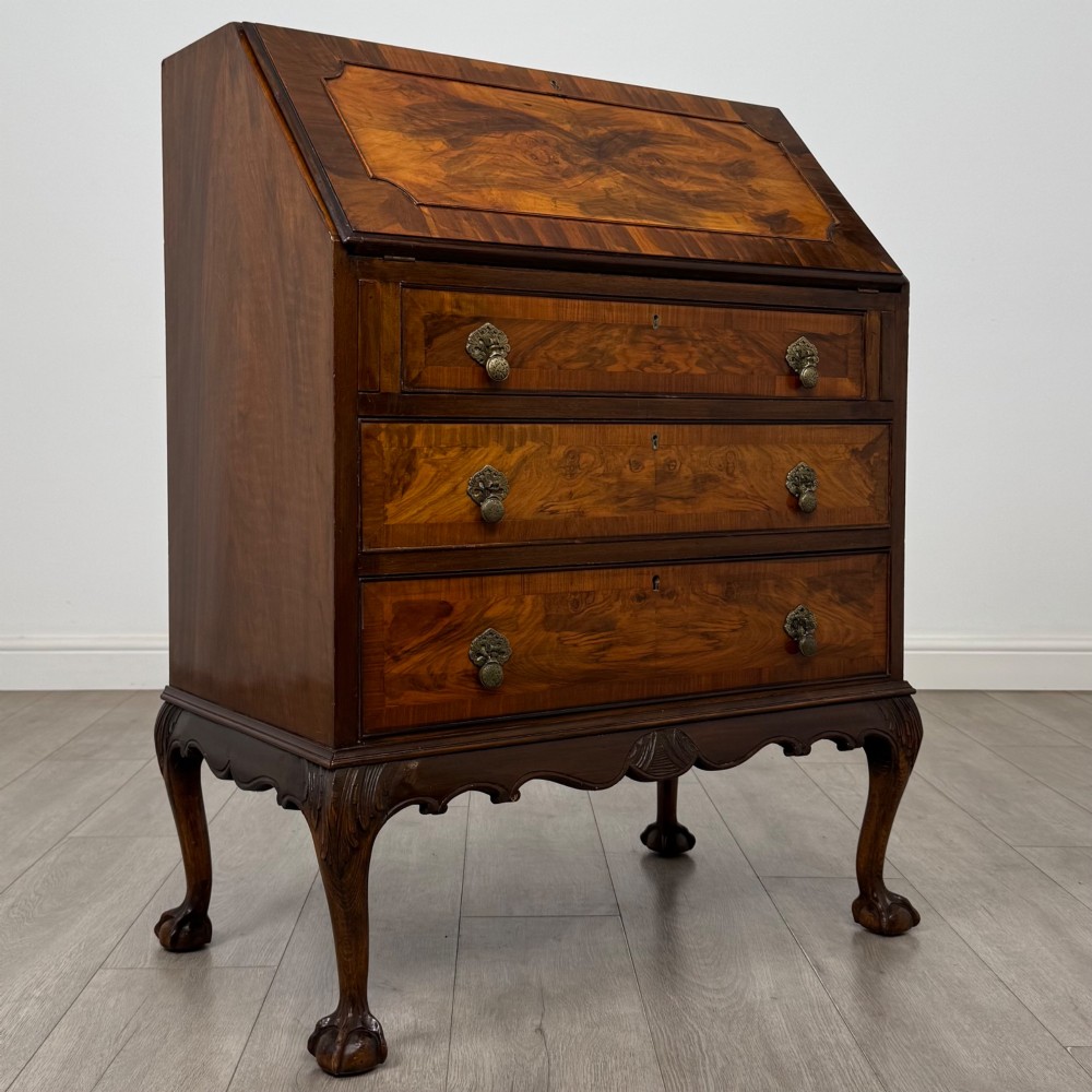 An antique Edwardian figured walnut writing bureau with a slant-front lid, three long drawers, brass handles, and carved cabriole legs on claw-and-ball feet. View IX