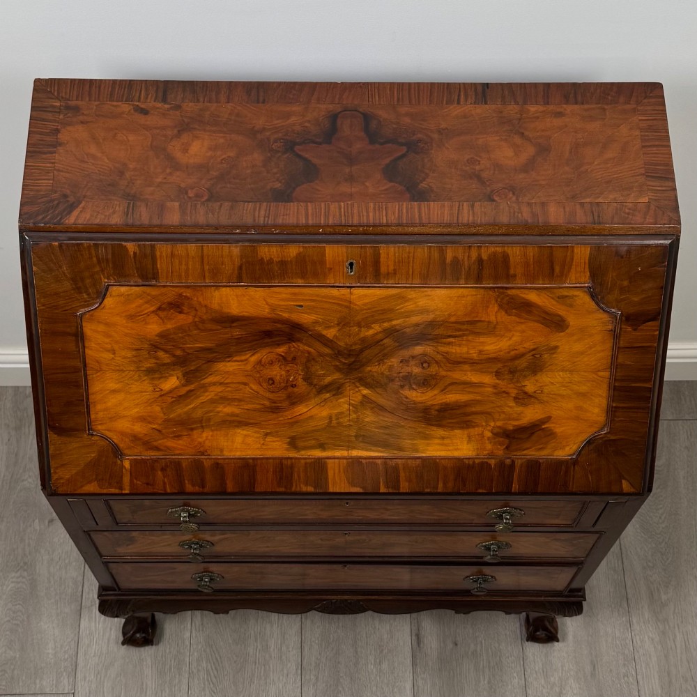 An antique Edwardian figured walnut writing bureau with a slant-front lid, three long drawers, brass handles, and carved cabriole legs on claw-and-ball feet. View X