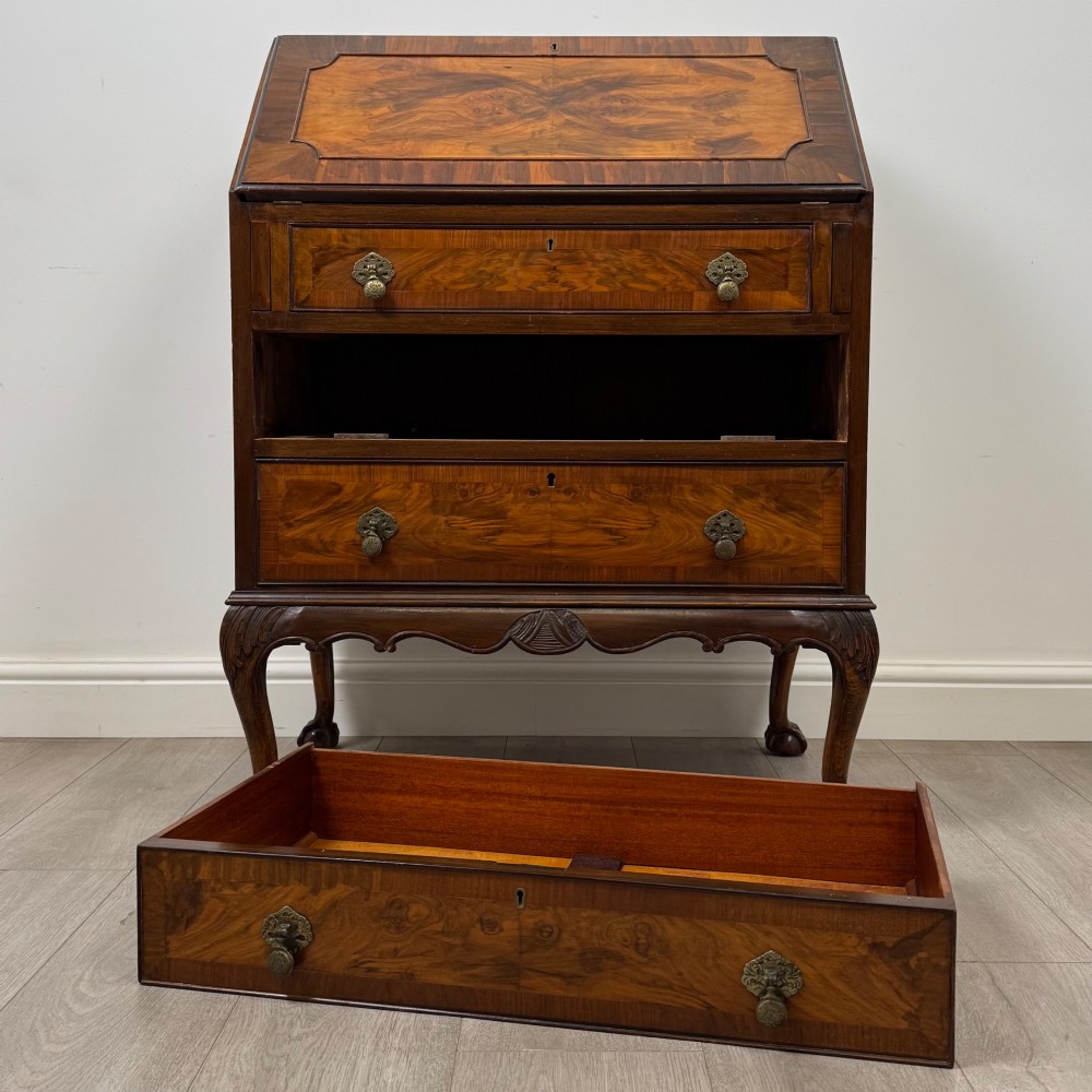 An antique Edwardian figured walnut writing bureau with a slant-front lid, three long drawers, brass handles, and carved cabriole legs on claw-and-ball feet. View XII