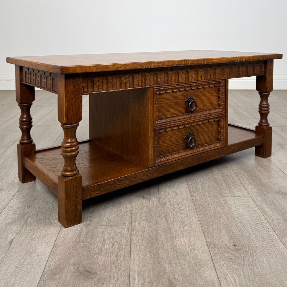 A rectangular carved oak coffee table with two central drawers, metal drop handles, turned legs, and a lower shelf. View IV