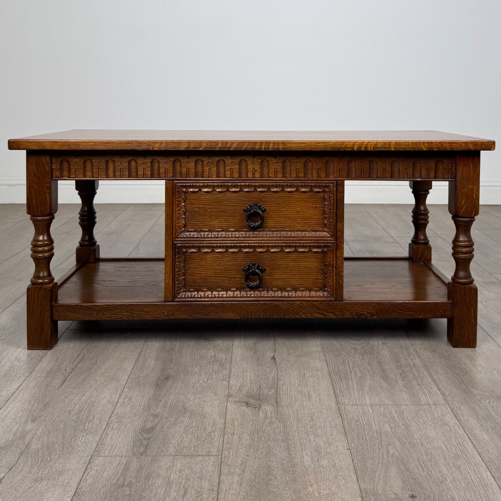 A rectangular carved oak coffee table with two central drawers, metal drop handles, turned legs, and a lower shelf. View V