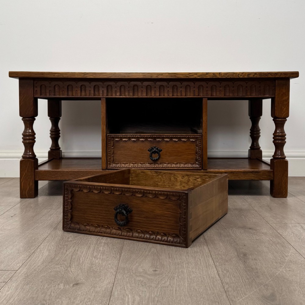 A rectangular carved oak coffee table with two central drawers, metal drop handles, turned legs, and a lower shelf. View X