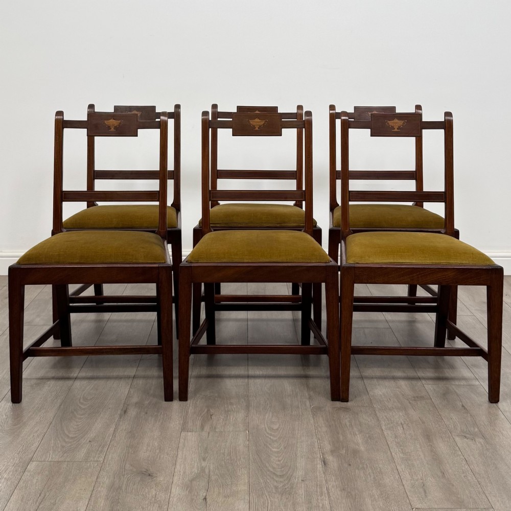 A set of six Georgian mahogany dining chairs featuring open rectangular backs with inlaid urn panels, straight legs with stretchers, and olive green velvet seats.
