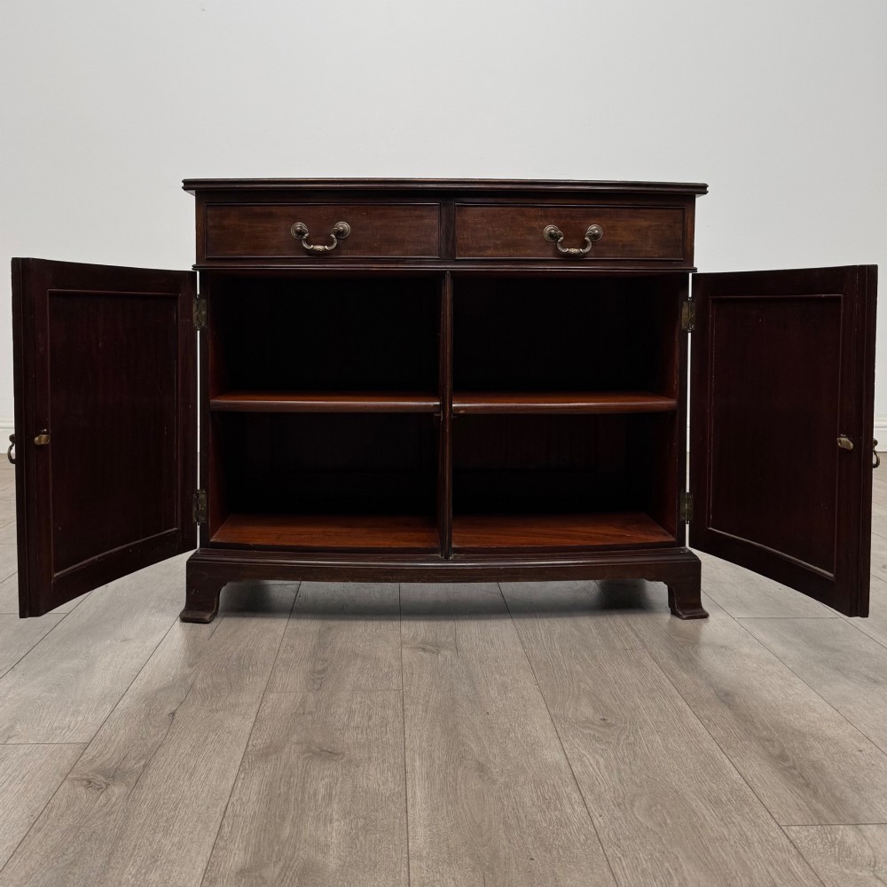 An antique Edwardian mahogany bow-front cupboard featuring two upper drawers with brass handles and two lower doors with oval wood grain panels. View II
