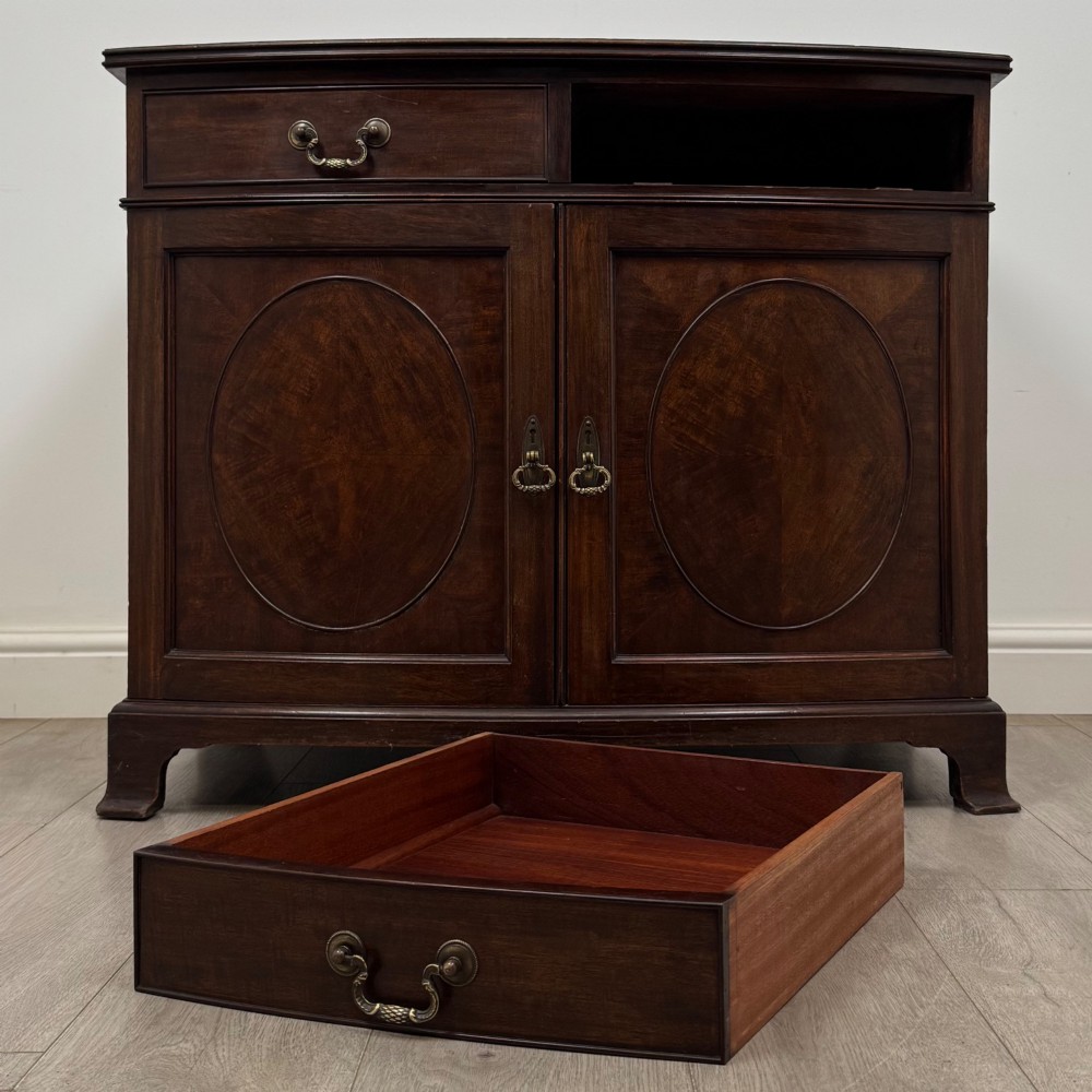 An antique Edwardian mahogany bow-front cupboard featuring two upper drawers with brass handles and two lower doors with oval wood grain panels. View XI