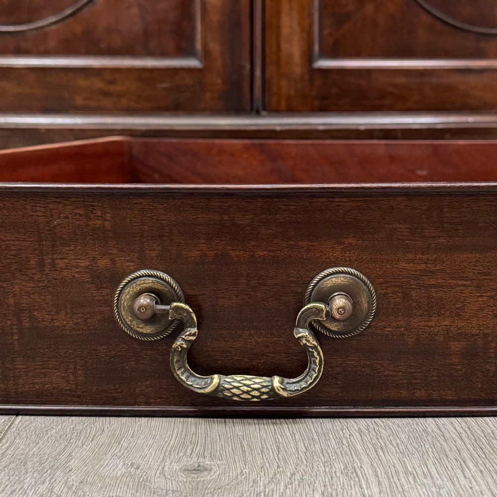 An antique Edwardian mahogany bow-front cupboard featuring two upper drawers with brass handles and two lower doors with oval wood grain panels. View XII