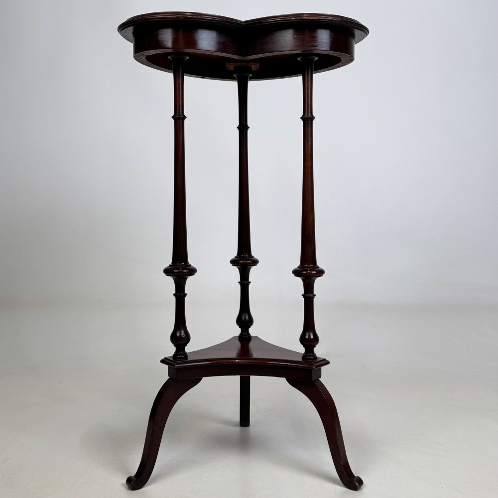 A tall dark mahogany side table featuring a heart-shaped top with a raised rim, three slender turned spindle legs, a lower triangular shelf, and flared feet.
