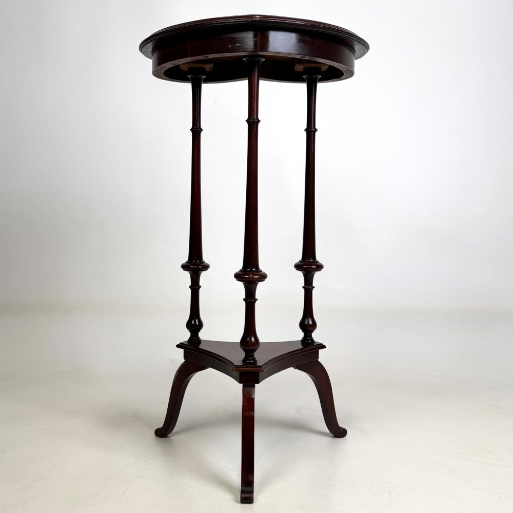 A tall dark mahogany side table featuring a heart-shaped top with a raised rim, three slender turned spindle legs, a lower triangular shelf, and flared feet. View II