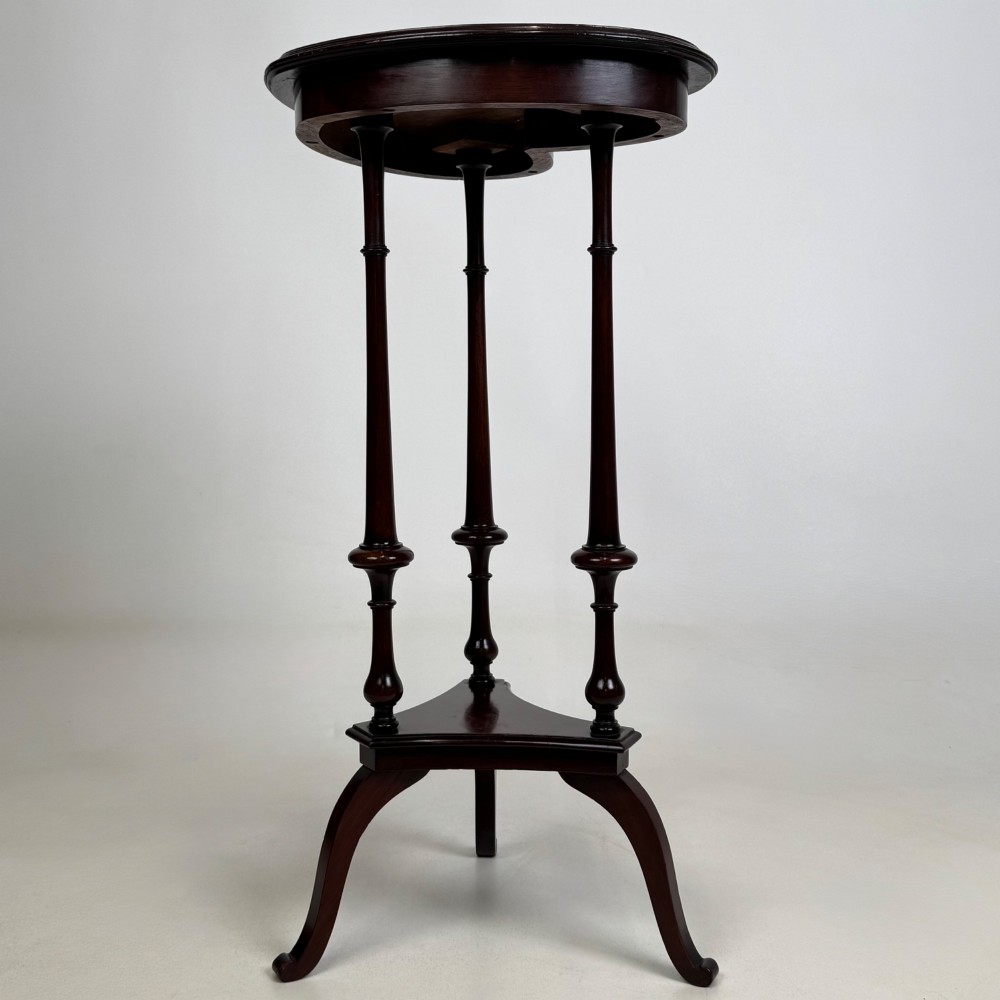 A tall dark mahogany side table featuring a heart-shaped top with a raised rim, three slender turned spindle legs, a lower triangular shelf, and flared feet. View III