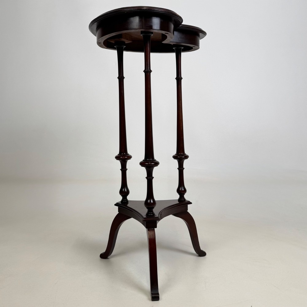 A tall dark mahogany side table featuring a heart-shaped top with a raised rim, three slender turned spindle legs, a lower triangular shelf, and flared feet. View IV
