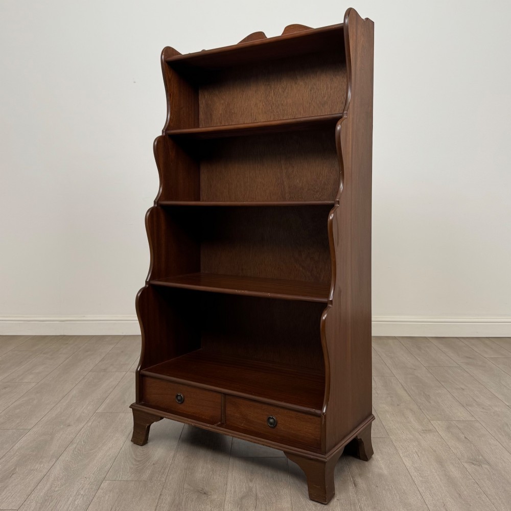 A freestanding dark mahogany waterfall bookcase with four graduated open shelves above two base drawers featuring ring pull handles. View III