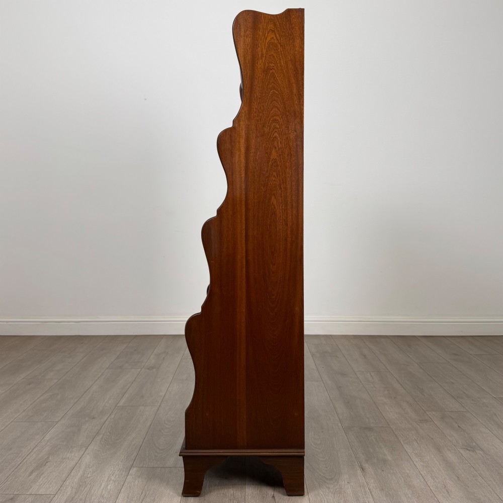 A freestanding dark mahogany waterfall bookcase with four graduated open shelves above two base drawers featuring ring pull handles. View IV