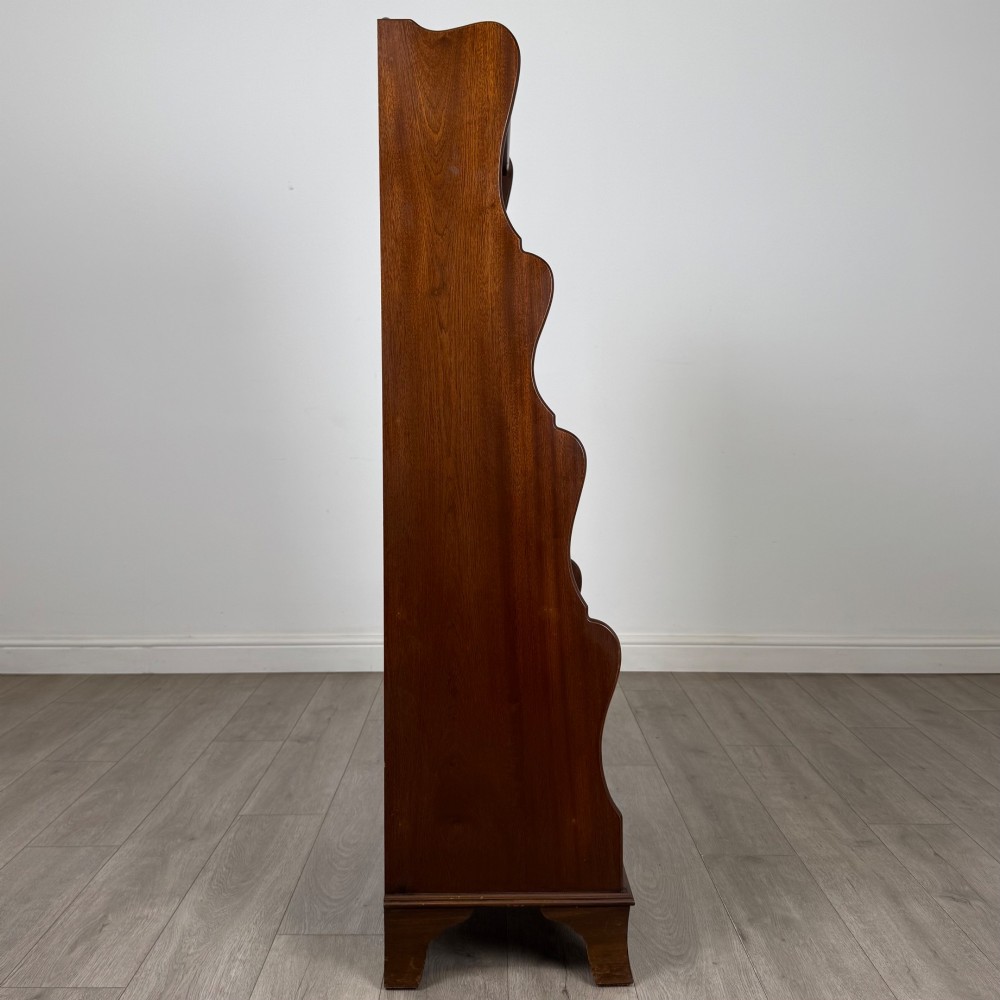 A freestanding dark mahogany waterfall bookcase with four graduated open shelves above two base drawers featuring ring pull handles. View VIII