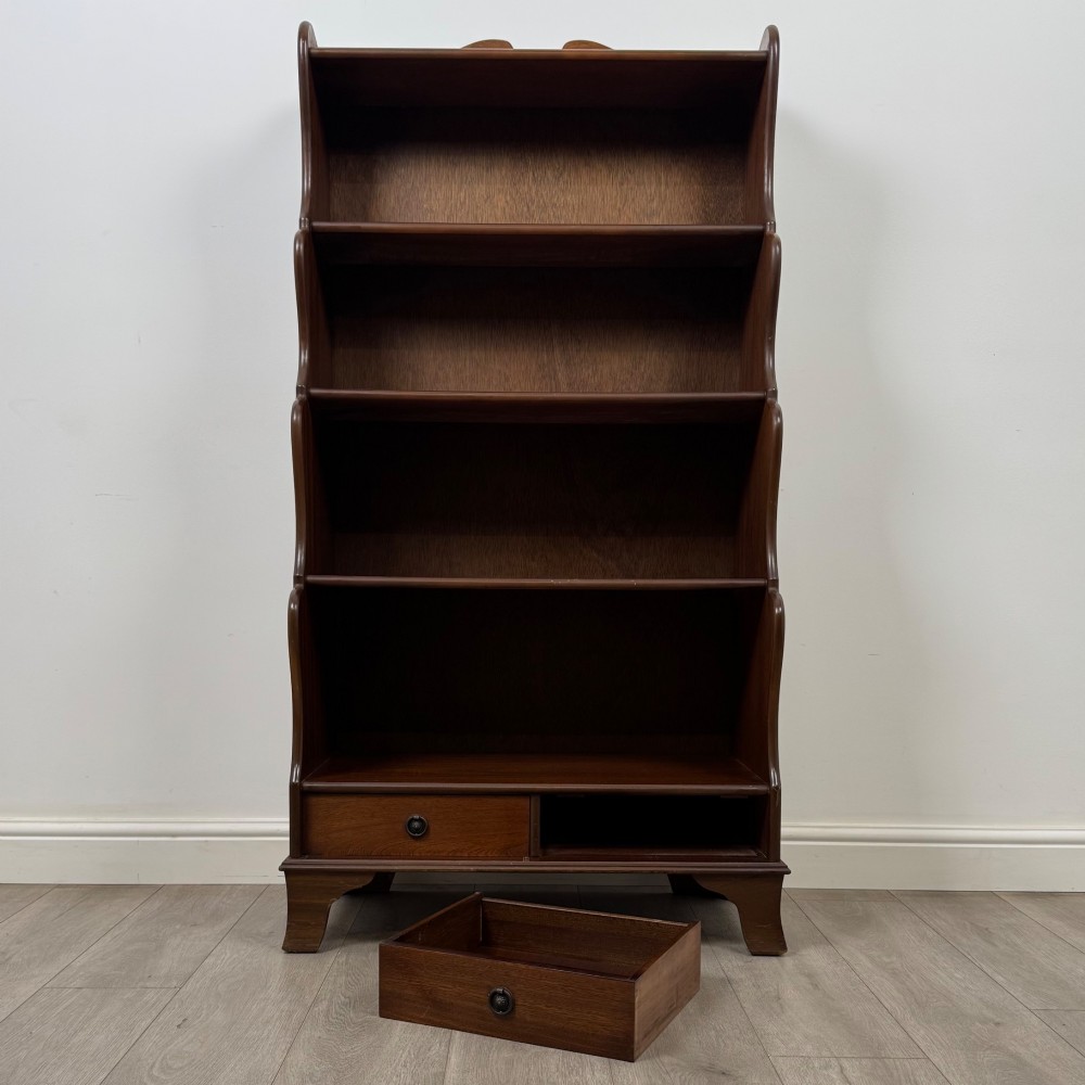 A freestanding dark mahogany waterfall bookcase with four graduated open shelves above two base drawers featuring ring pull handles. View XI